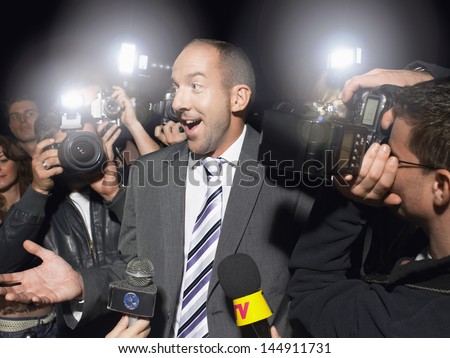 Surprised man in suit surrounded by paparazzi