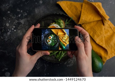 Girl taking photo of sandwich with eggs with smart phone at dark background. instagram photography blogging workshop concept. Royalty-Free Stock Photo #1449124670