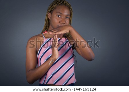 Young pretty African American girl tired and bored, making a timeout gesture, needs to stop because of work stress, time concept. Standing against gray wall.