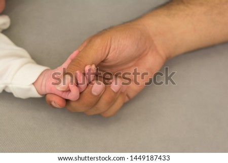 close up photo of father's hand holding his newborn son hand  ,Picture taken on a gray background.