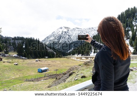 beautiful young woman with red hair photographer takes a picture of a mountain landscape on the phone while hiking