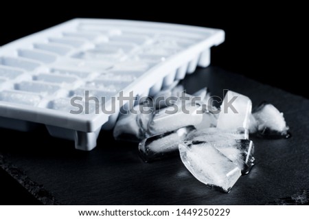 frozen ice cubes and forms for a refrigerator on a stone plate on a black background, isolate