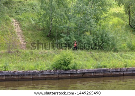 Young girl in a baseball cap runs along the river in a green summer forest