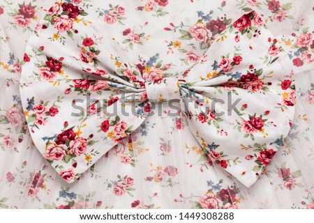 Full frame bow on floral pattern dress detail, extreme close up fashion concept backgrounds. Red flowers on white cotton fabric sewing background, romantic fashion and style clothing, textile industry