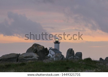 Lighthouse behind huge rocks. The beacon stands behind big rocks on the coast in Brittany in France. The sky is full of clouds and the sun is just setting. It is a good night picture.