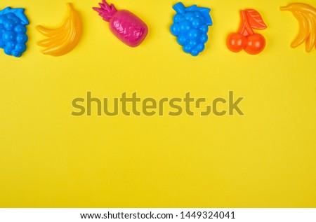 multicolored plastic toys fruits on a yellow  background, copy space 