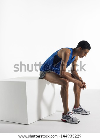 Full length side view of a male athlete sitting on box against white background