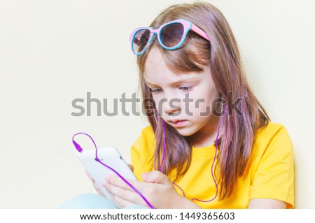 The child sits in the room and listens to music. Little girl in a yellow T-shirt and glasses. Hot sunny summer. Horizontal