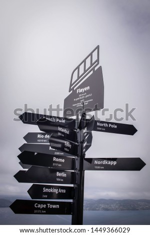 A black and white photograph of a sign that has distances to each city in Bergen, Norway.  
