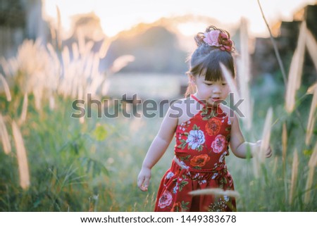 Asian little girl in red dress, walking like Happy in the flower garden and sunset. Outdoor Kids Fashion .Sweet toddler girl with floral head wreath on and flowers bunch in hands 