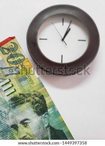 approach to Israeli banknote of twenty shekels and background with a circular wall clock