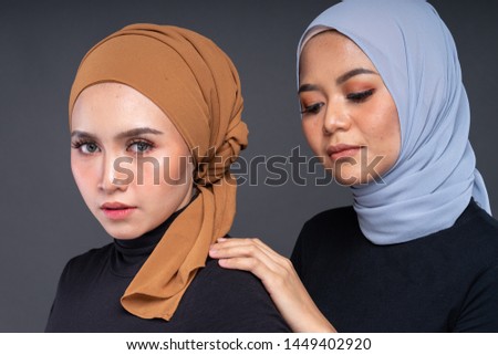 Close up portrait of a beautiful Muslim female models wearing sweatshirt with hijab isolated over grey background. Studio fashion and beauty make up concept.
