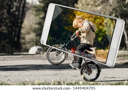 Smartphone displaying photo of little boy doing a wheelie in city park, smart device concept