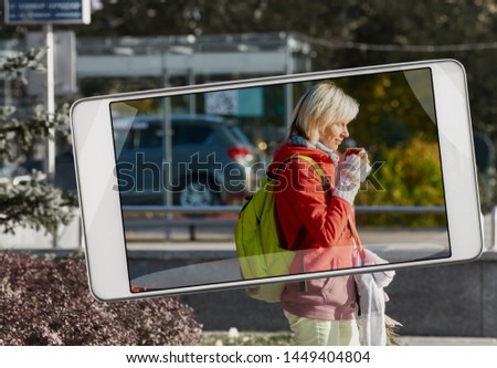 Portrait of young attractive woman drinking coffee in city street, concept of new features of smart device