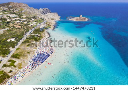 Stunning aerial view of the Spiaggia Della Pelosa (Pelosa Beach) full of colored beach umbrellas and people sunbathing and swimming in a beautiful turquoise clear water. Stintino, Sardinia, Italy. Royalty-Free Stock Photo #1449478211