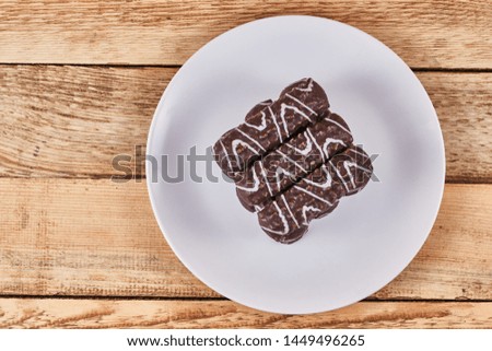 Long sticks shortbread cookies in dark chocolate icing on a white plate on wooden background. Flat lay