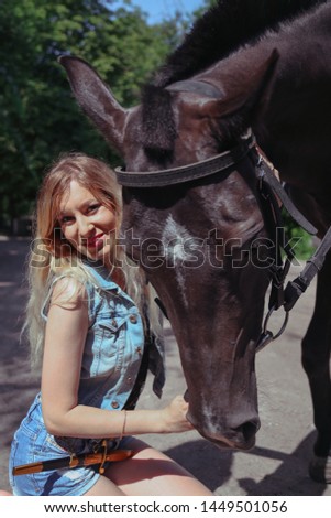 Cute girl blonde with a dark beautiful horse. Photo session of a young girl with a horse.