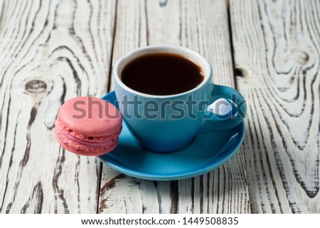 Full ceramic cup of hot black coffee near sweet pink macaroon on old weathered rustic white table. Copy space