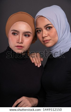 Close up portrait of a beautiful Muslim female models wearing sweatshirt with hijab sitting on a chair isolated over grey background. Studio fashion and beauty concept.