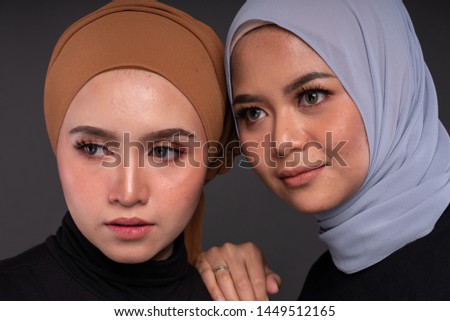 Close up portrait of a beautiful Muslim female models wearing sweatshirt with hijab sitting on a chair isolated over grey background. Studio fashion and beauty concept.