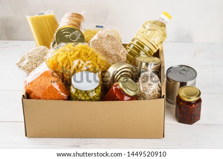 Various canned food, pasta and cereals in a cardboard box. Food donations or food delivery concept. Royalty-Free Stock Photo #1449520910