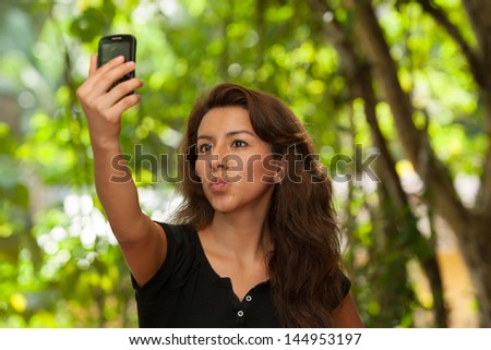 Young attractive Hispanic woman portrait outside green behind taking her own picture