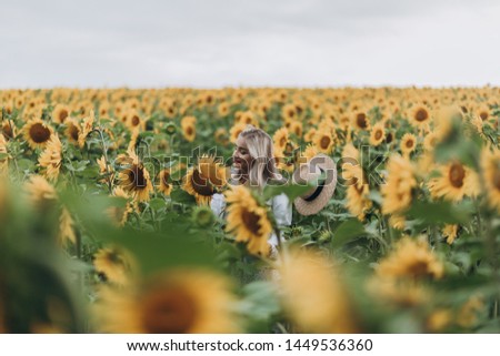 Young beautiful stylish blonde mother in a country dress and hat walks in the field of sunflowers, having fun, laughing