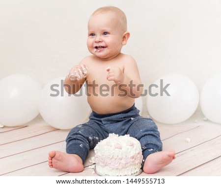 Funny one year baby birthday party. Baby eating birthday cake. The boy on a light background celebrates and smash the cake.