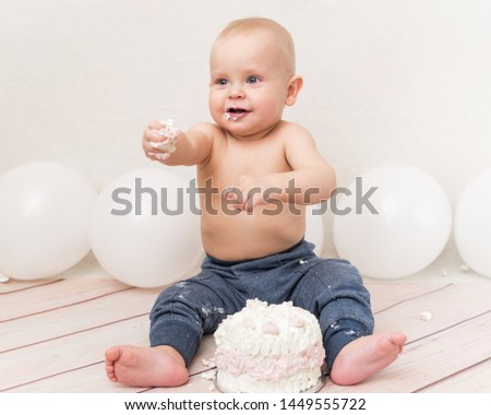 One year baby birthday party. Baby eating birthday cake. The boy on a light background with ballons celebrates and smash the cake.
