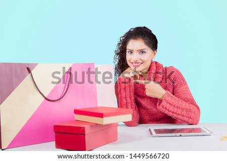 Picture of a young woman smiling at the camera while pointing shopping bags in the studio
