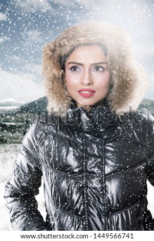 Picture of pensive woman wearing winter jacket while standing in the snowy park