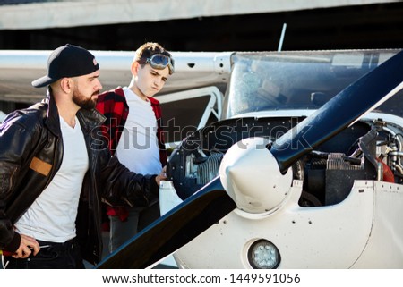 father and son standing together, looking at light propeller airplane engine thoughtfully, searching for reason of breakdown, going to fix the mechanism. Aviation concept.
