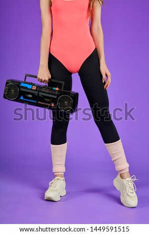 athletic fitness woman in perfect shape, standing in pink bodysuit, black leggins and white training shoes, close up on legs and portable radio cassette player