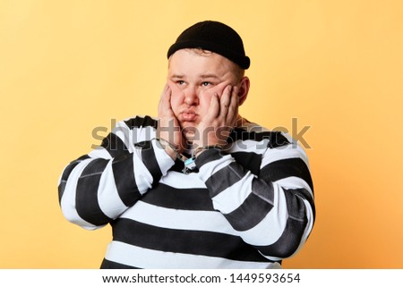 plump pensive criminal holding his cheeks and looking away, isolated yellow background, studio shot.