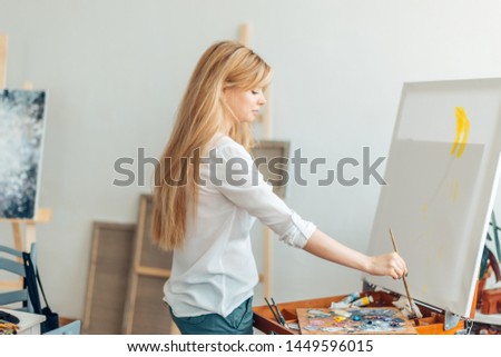 fair-haired woman painting with a brush in the art classes. close up side view photo. hobby, lifestyle, free time