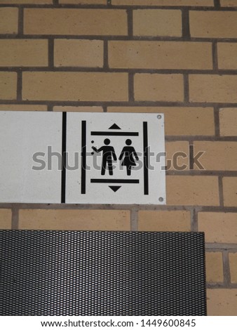 Funny sign of a man and a woman for a lift in a train station with brick wall