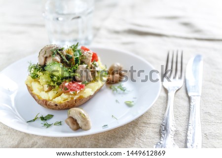 Whole baked potato with mushrooms, tomatoes and vegetables. Serving on a white plate on a light rustic fabric background. Close-up. Top view. Copy space