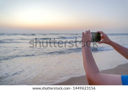 Hands of young indian woman holding up a phone to click a picture of a beautiful beach in gujarat india. These beaches are a favorite spot for tourists and visitors and are often filled with