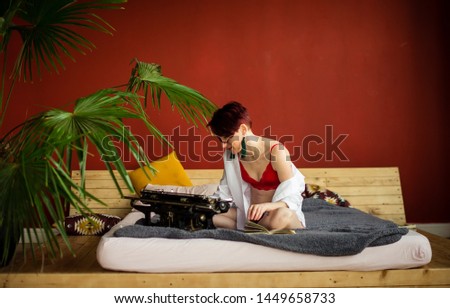 
A young, beautiful woman in red underwear prints on a typewriter