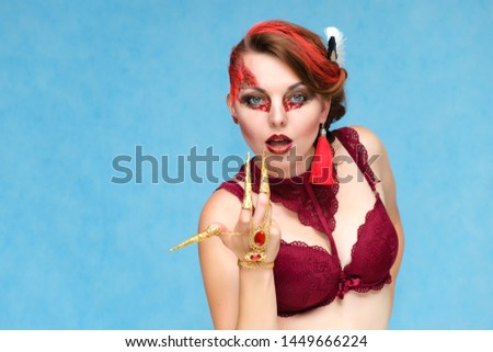 Portrait waist-up against a blue background of a pretty young brunette woman with beautiful makeup, with gold jewelry on her hand. Art, beauty, great makeup. Shows emotions.