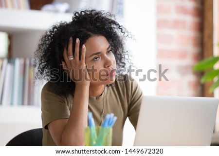 Bored African American businesswoman disinterested in routine monotonous work, unmotivated female employee or student holding head on hand, rolling eyes, using laptop at workplace, close up Royalty-Free Stock Photo #1449672320