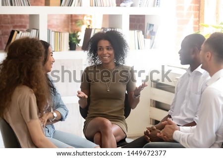 Smiling African American psychologist counselling, speaking with diverse people sitting in circle at group therapy session, business coach training staff, having fun, team building activity at work Royalty-Free Stock Photo #1449672377