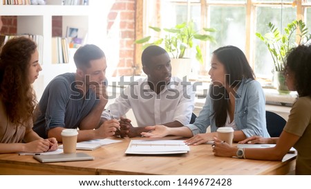 Horizontal photo diverse employees team discussing project at meeting, colleagues listening to Asian businesswoman, colleagues sitting at office table, students study together in classroom or library