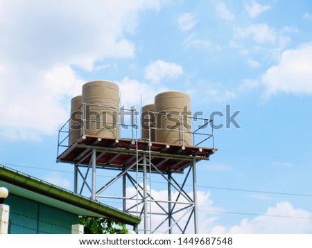 Plastic water tank on the tower Water tanks are made of cream-colored plastic for storing water used in villages or farms. On a blue sky background with white clouds with a copy area. selective focus
