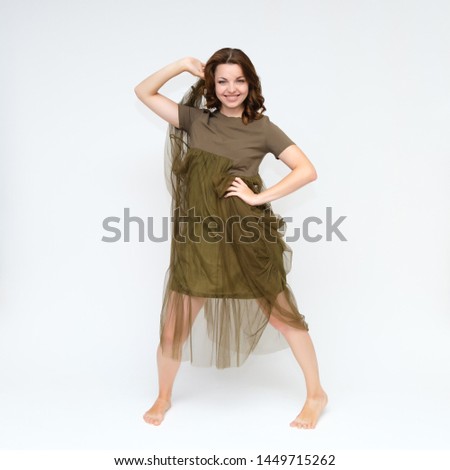 Portrait in full growth on a white background pretty young brunette woman in a green dress with beautiful hair. Standing in different poses, talking, showing hands, demonstrating emotions.