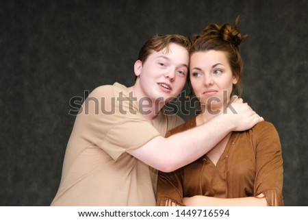 A portrait below the belt on a gray background of a pretty young brunette woman in a brown dress and a young man in a brown shirt. They stand in different poses, talking, showing emotions.