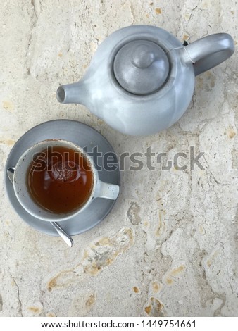 teapot with tea in teacup and saucer on marble table