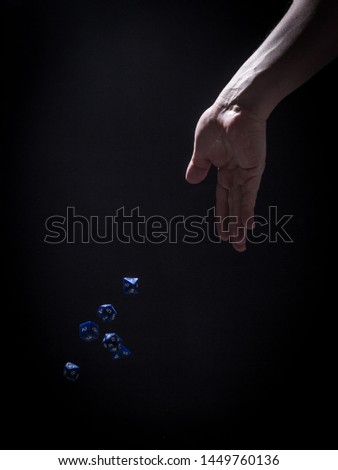 A Caucasian Man's Hand Tossing Blue Role Playing Dice - with a Black Background