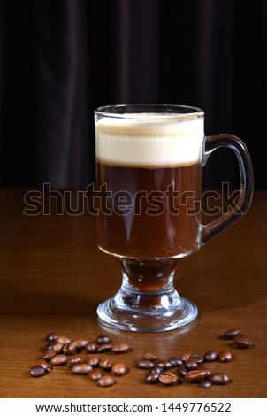 Irish coffee in a glass cup on a wooden table. Dark background.