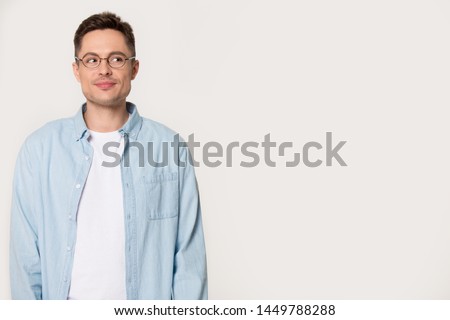 Young millennial man with cunning look isolated on grey background. Thoughtful mysterious male looking aside wearing glasses posing at studio. Advertising, blank, empty copy space banner concept